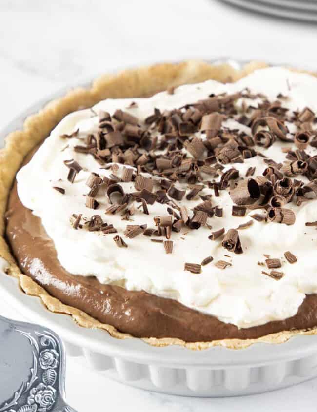 a close up of a chocolate pudding pie topped with whipped cream and chocolate shavings