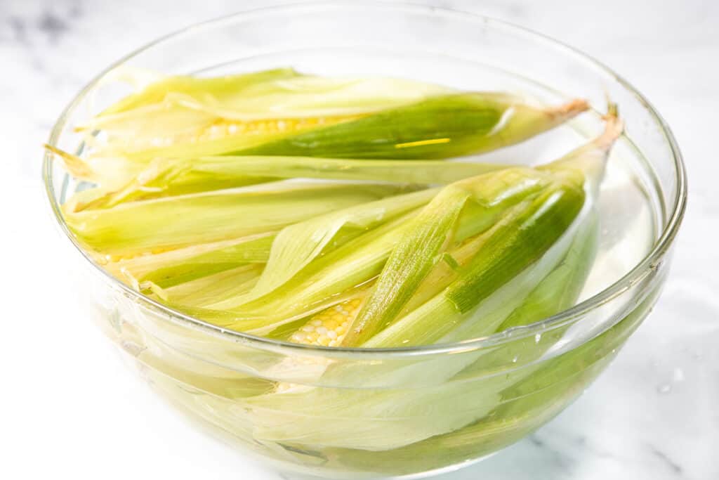A bowl with water covering ears of corn
