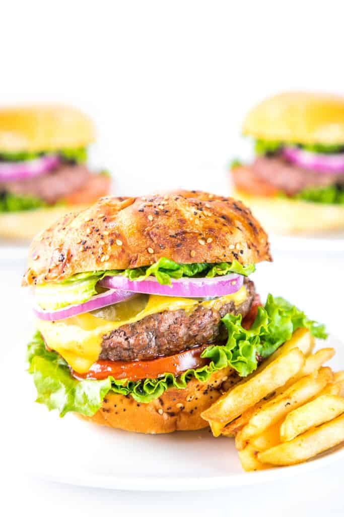 Three burgers made with The Best Hamburger Recipe topped with onions, pickles, cheese, tomatoes, and lettuce.