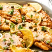 A plate of Fish Piccata garnished lemon and capers.