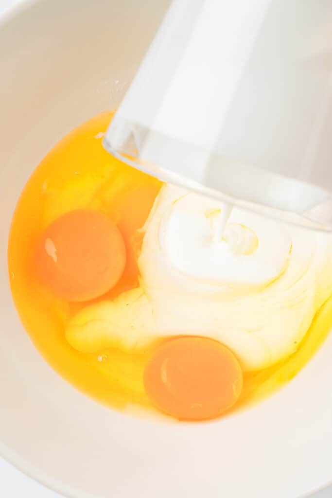 milk being poured into a bowl with eggs.