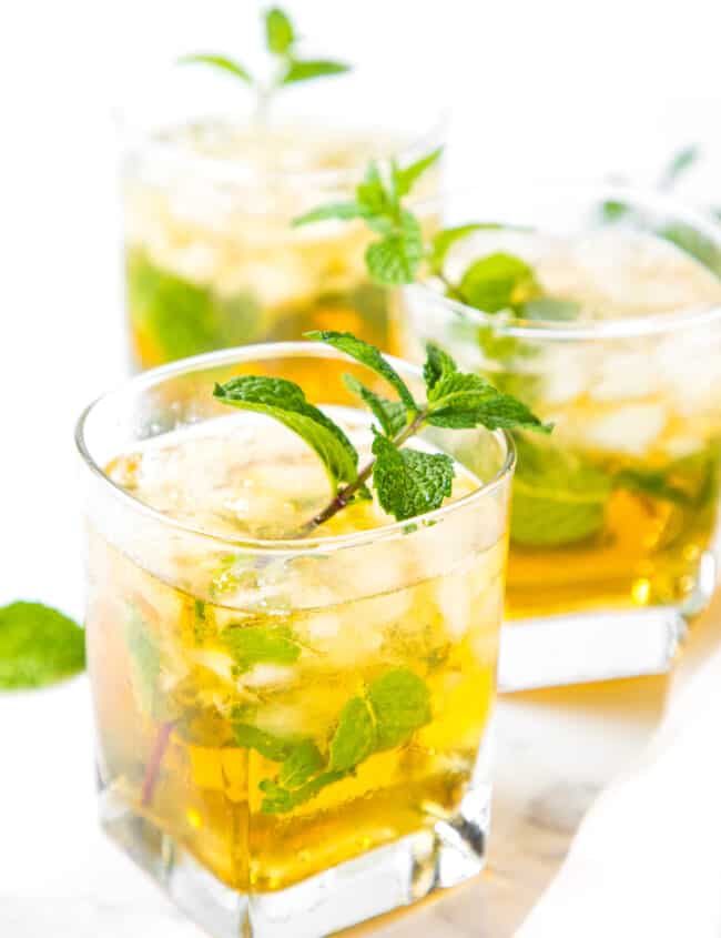Three mint juleps in rocks glasses garnished with a sprig if mint