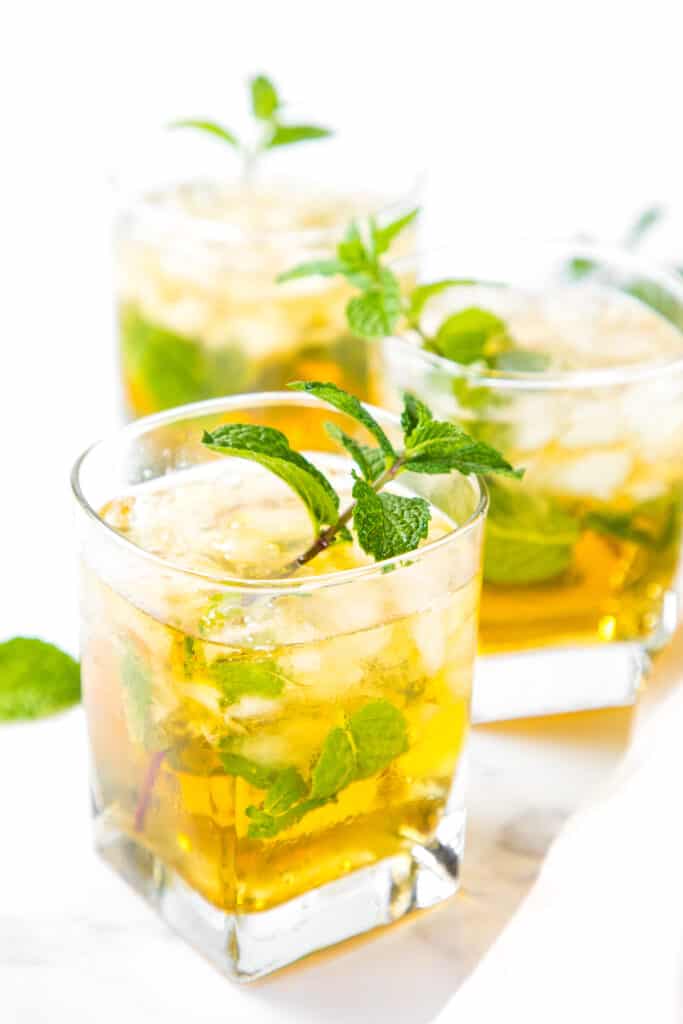 Three mint juleps in rocks glasses garnished with a sprig if mint