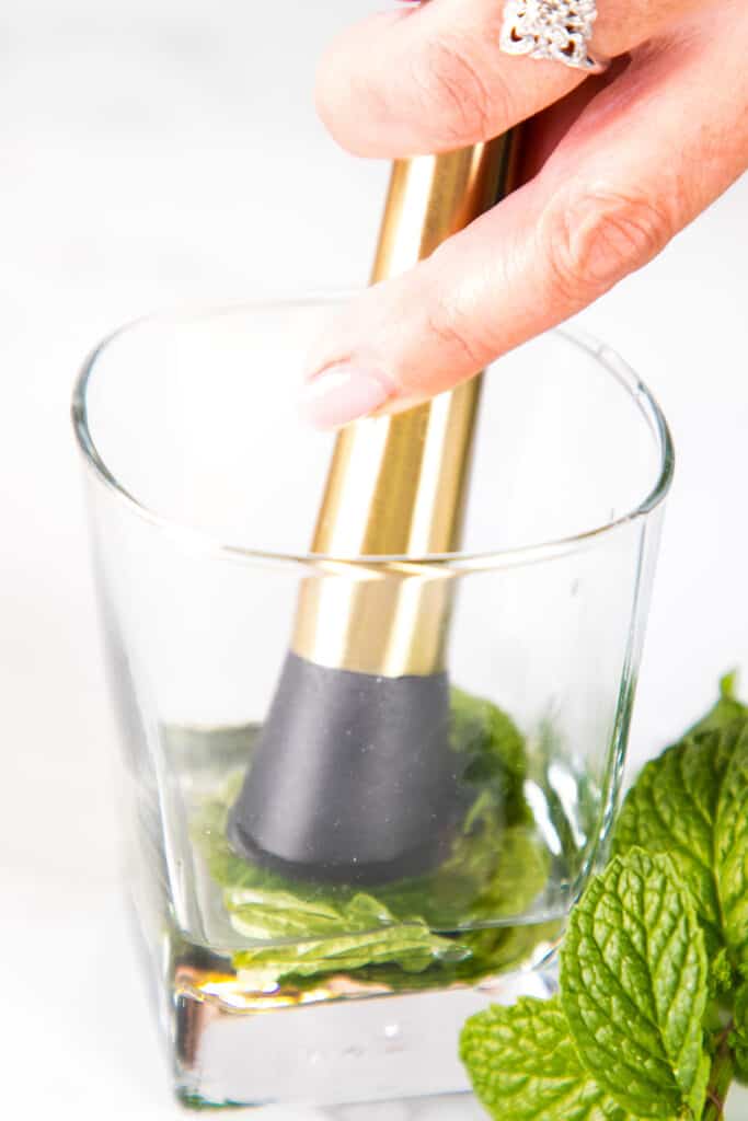 a muddler pressing mint leaves into simple syrup