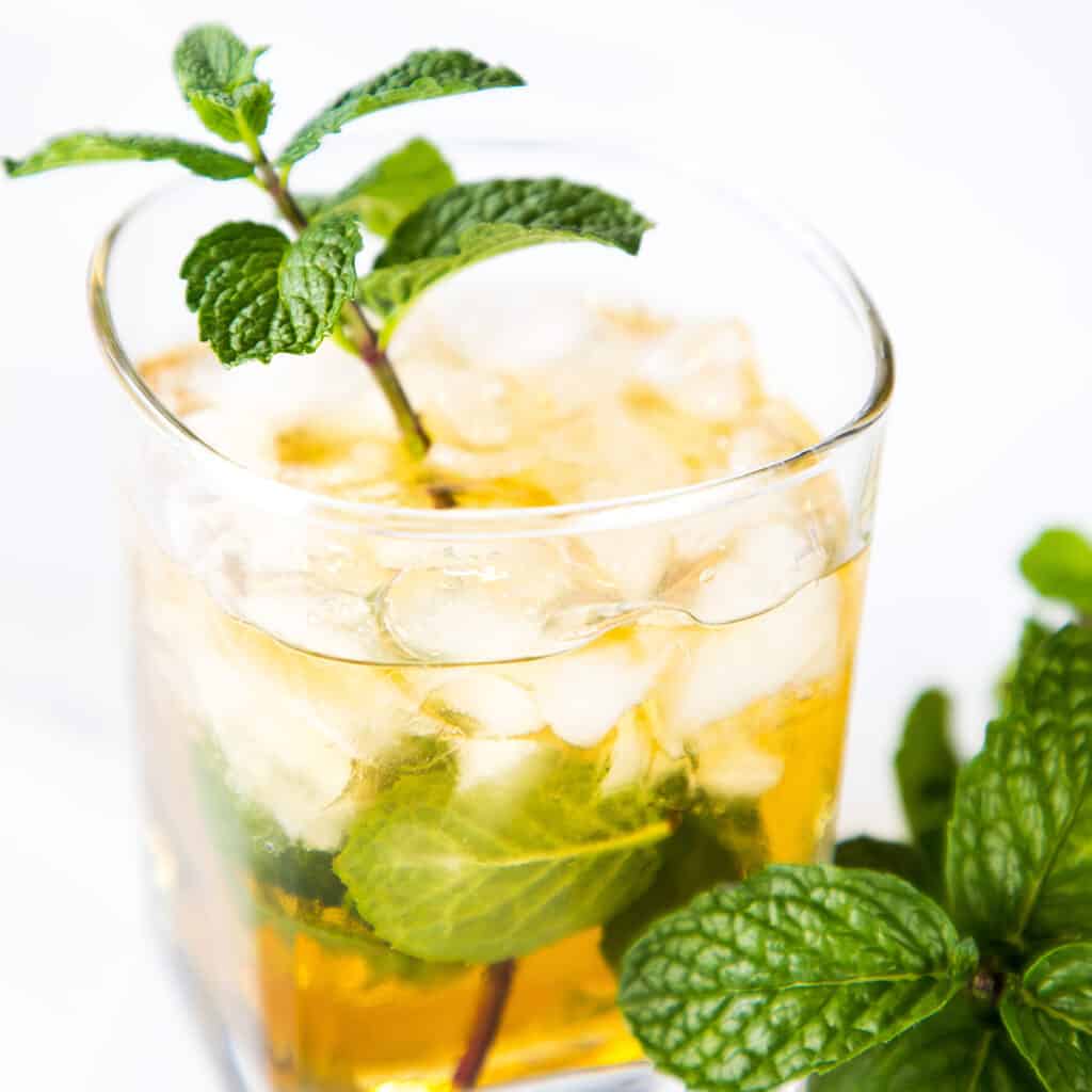 A mint julep cocktail garnished with a sprig of mint with more mint next to the glass