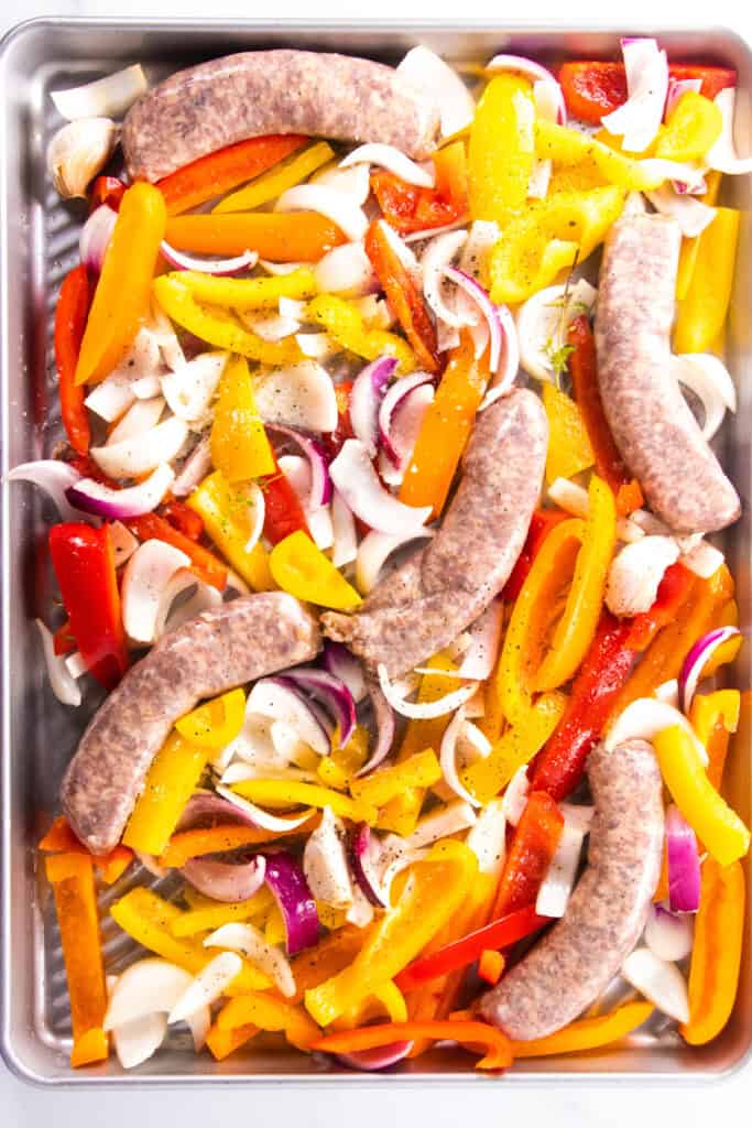 a baking sheet with onions, peppers and sausage seasoned with salt and pepper