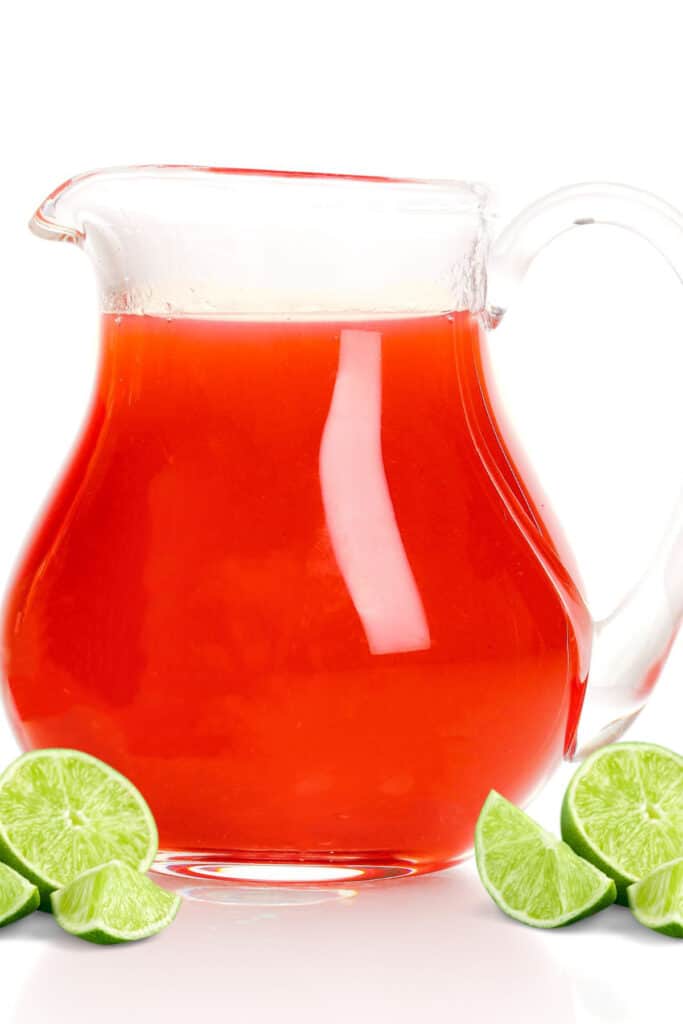 a pitcher of sea breeze cocktails with lime wedges next to it