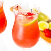 Two sea breeze cocktails with a garnish of cherries and lime slices with more fruit in the background.