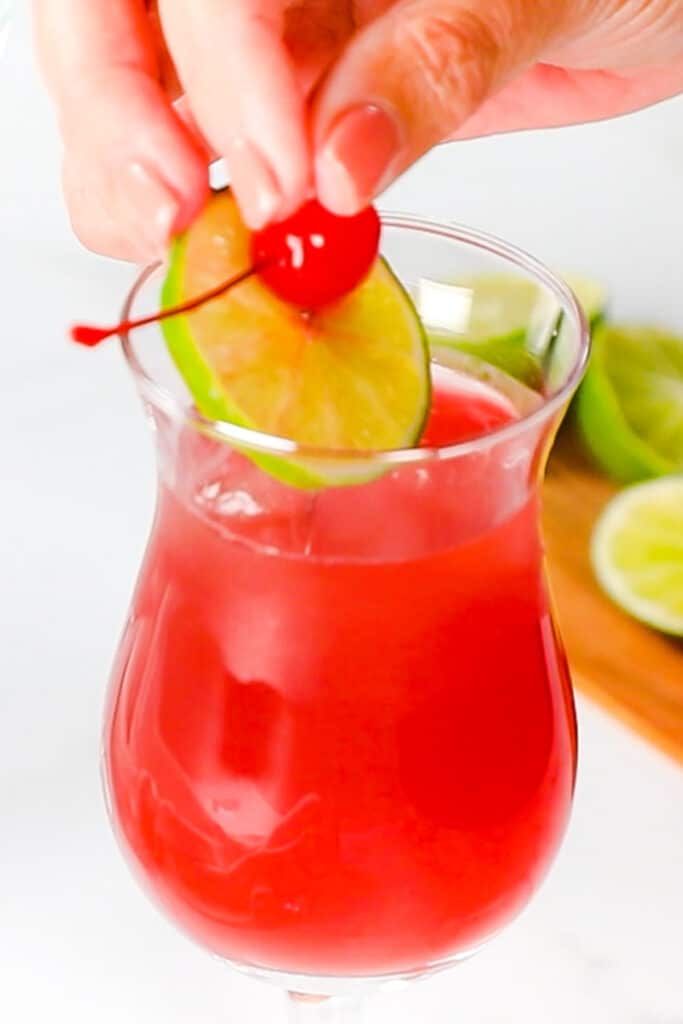 a maraschino cherry and lime slice being placed in a sea breeze cocktail