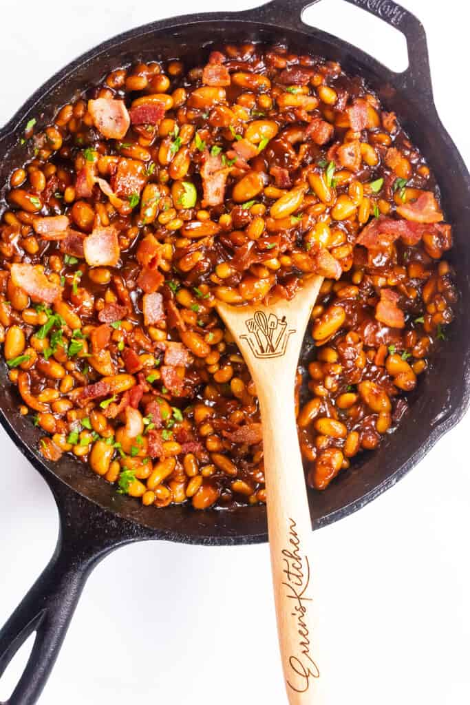a black pan of Homemade BBQ Baked Beans with a serving spoon