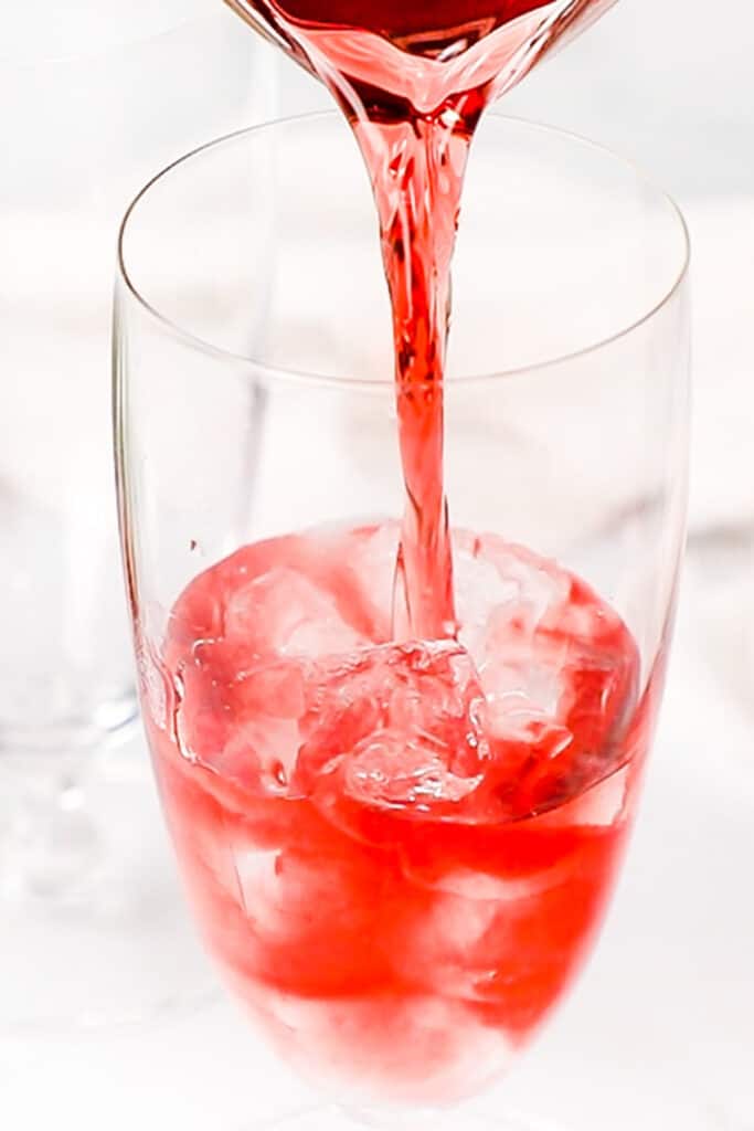 cranberry juice being poured into a glass with ice and vodka