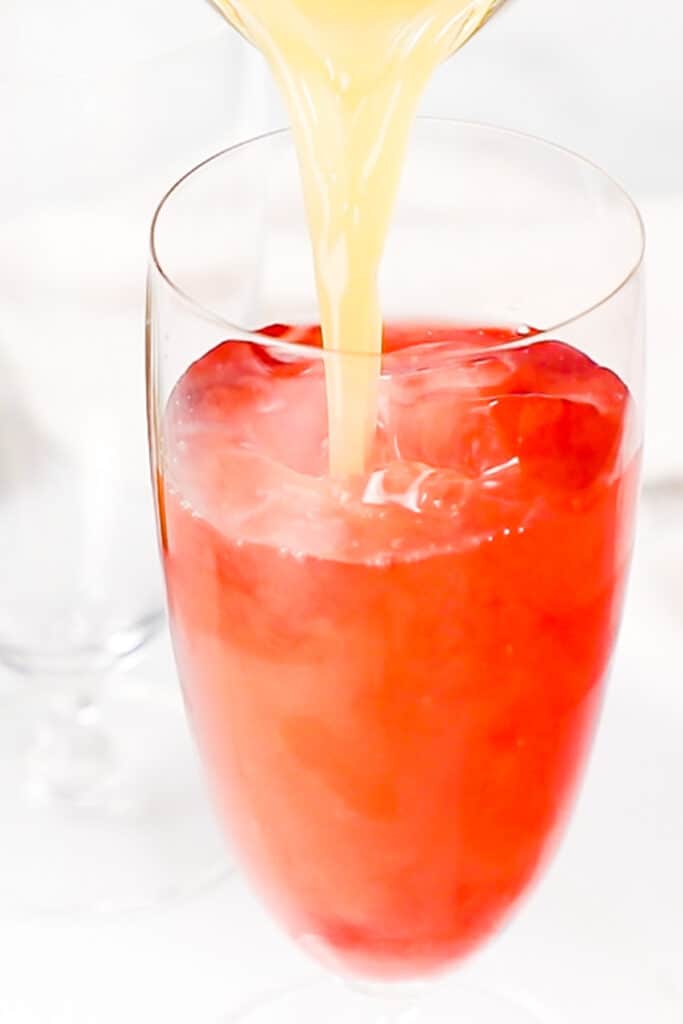 Pineapple juice being poured into the cranberry and vodka mixture