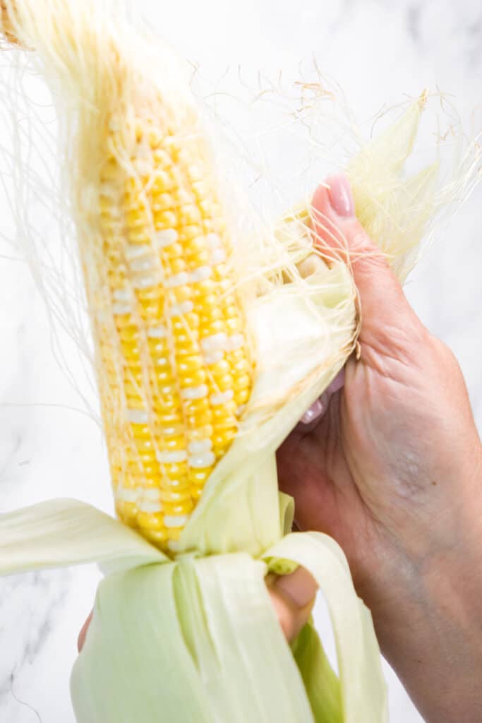 The husk being pulled from an ear of corn