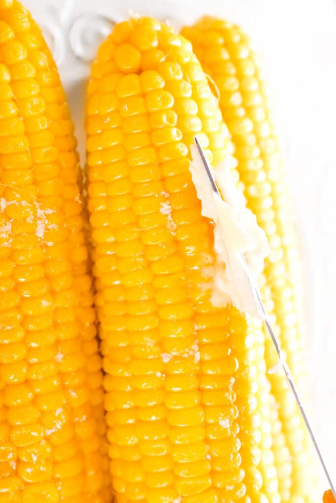 Plate with boiled corncobs and butter on table, closeup