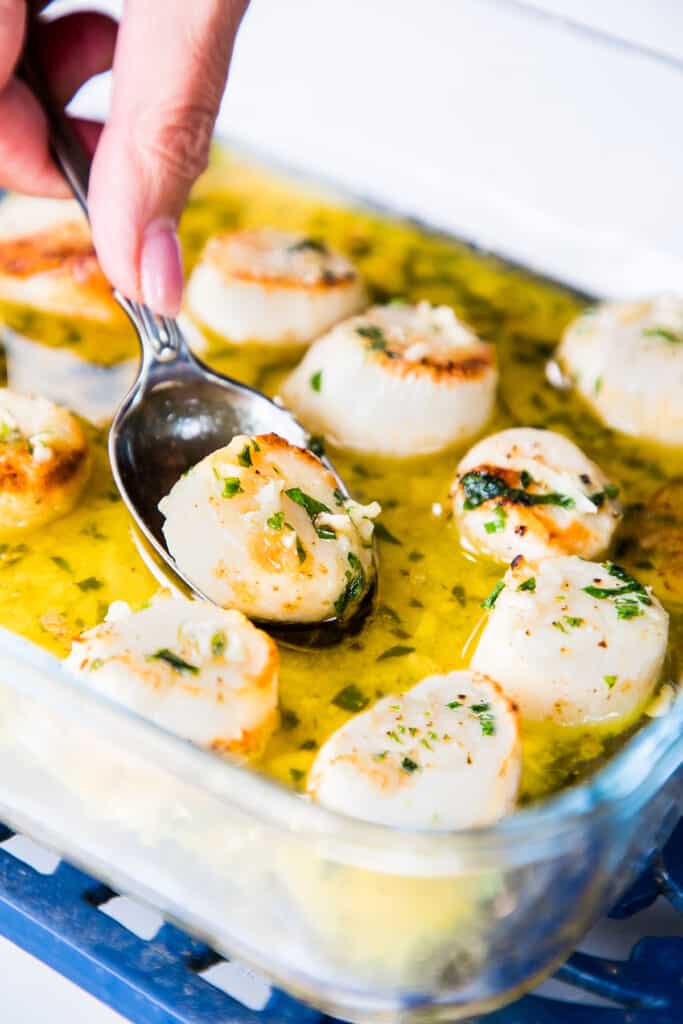 a tray of broiled scallops with garlic butter being served with a spoon