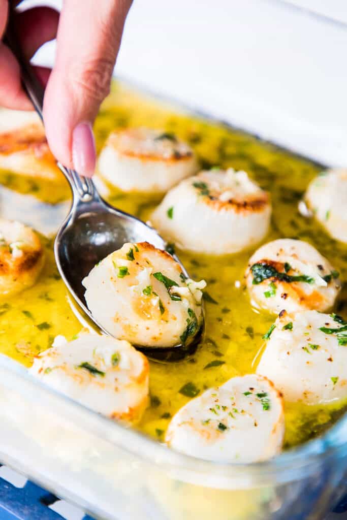 broiled scallops in a garlic butter sauce being served with a spoon