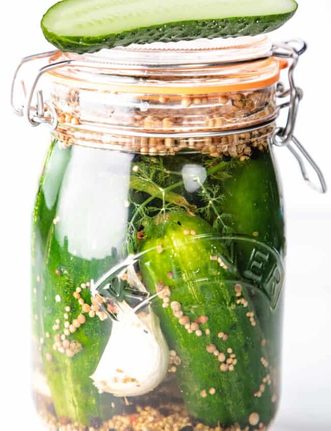 a jar of Half Sour Refrigerator Pickles with one halved pickle on top of the jar