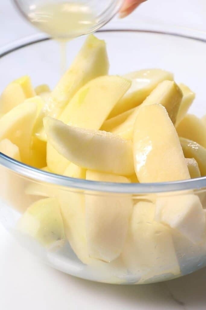 lemon juice being poured into a bowl of apples