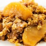 A close-up of Oatmeal Apple Crisp shows baked apple slices coated in cinnamon, sugar, and oats, with a golden-brown crumbly topping on a white plate.