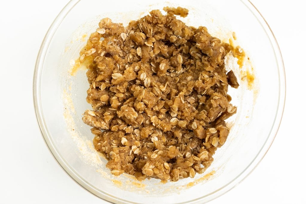 A glass bowl filled with an oatmeal cookie dough mixture, featuring oats and brown sugar reminiscent of a classic Oatmeal Apple Crisp, on a white background.