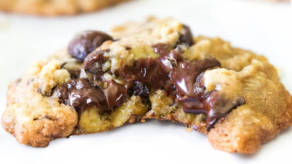 Close-up of a gooey chocolate chip cookie with melted chocolate oozing from the center. The easy chocolate chip oatmeal cookie appears freshly baked, with a golden-brown, slightly crispy exterior.