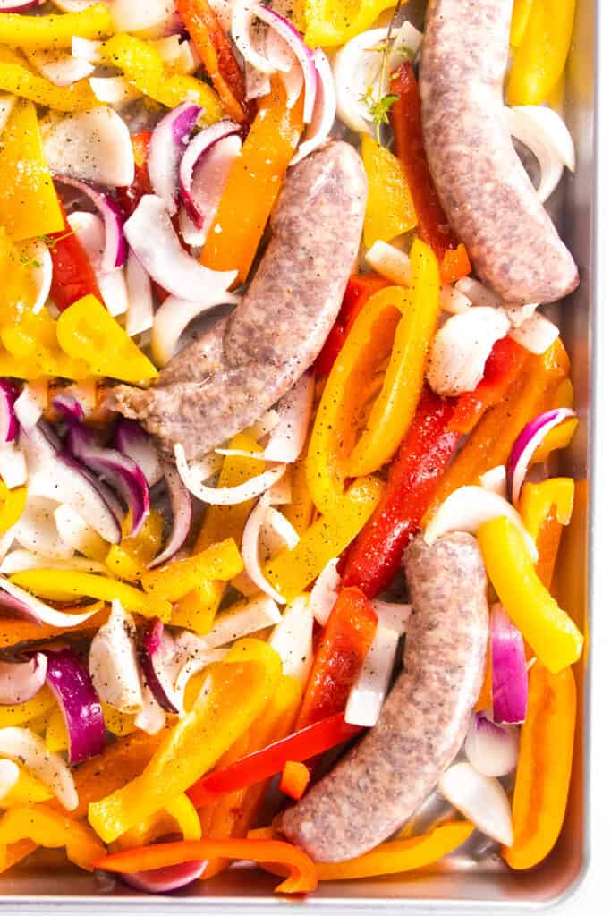 sausage, onions, peppers and garlic spread onto a sheet pan