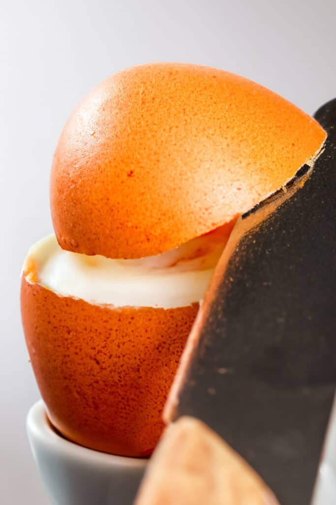 a knife cutting through the top of a cooked egg