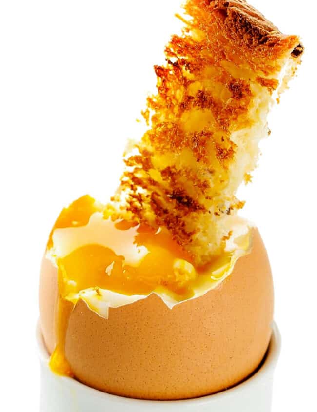 a soft boiled egg in an egg cup with a strip of toast dunking into the yolk.