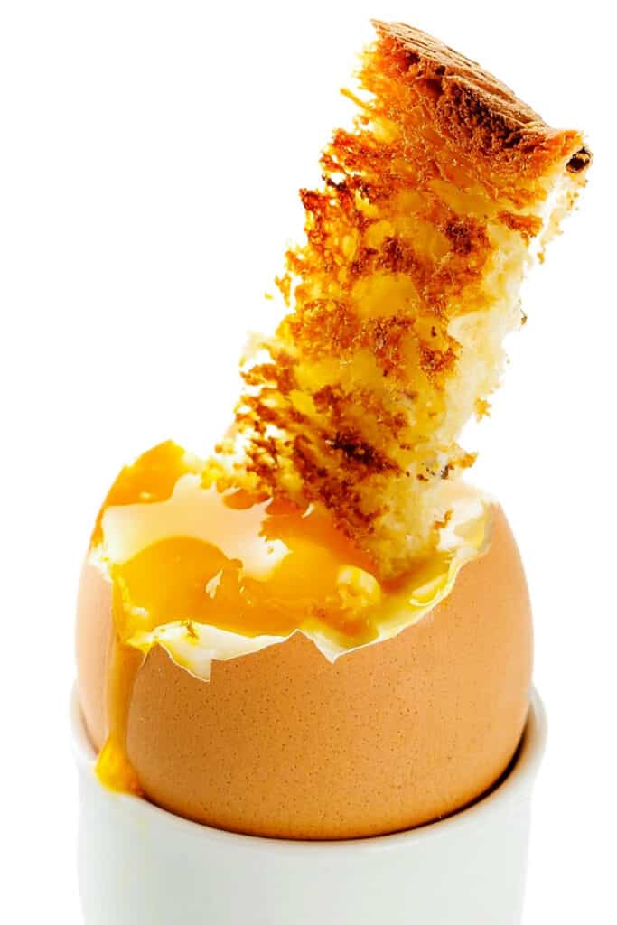 a soft boiled egg in an egg cup with a strip of toast dunking into the yolk.