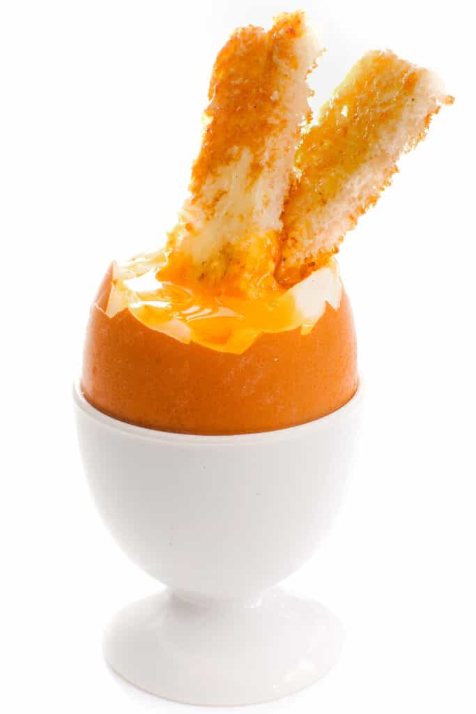 a soft boiled egg in an egg cup with two strips of toast in the yolk