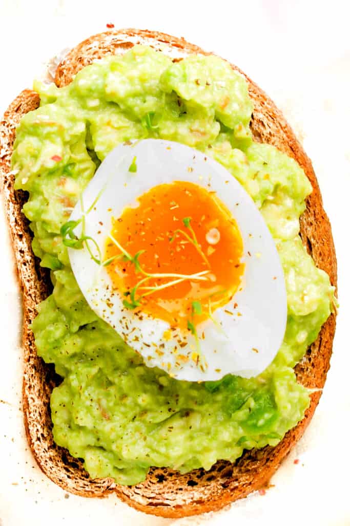 Toast with Guacamole and soft boiled egg on a white plate with a fork next to it.