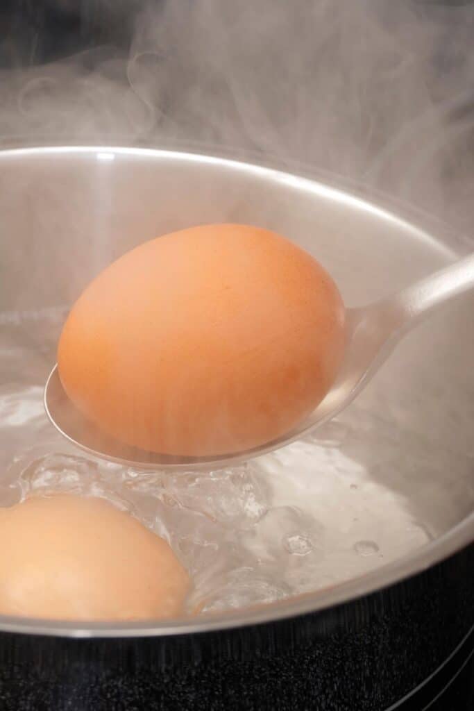 una cuchara bajando un huevo en una olla de agua hirviendo