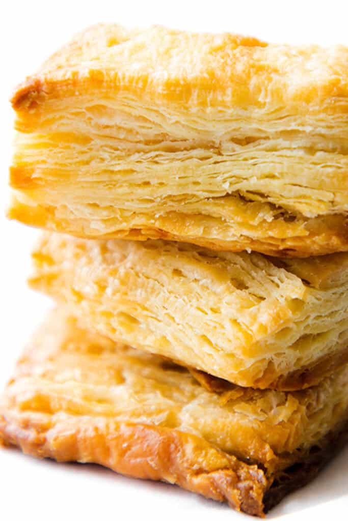 a close up image of three slices of baked, golden rough puff pastry