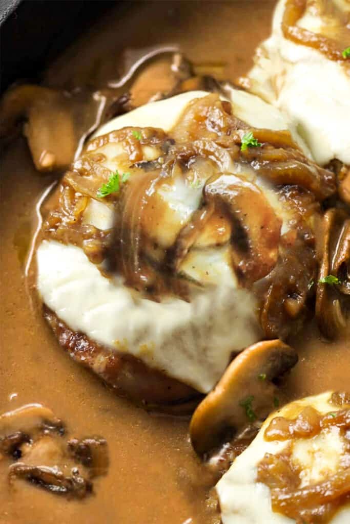 a pork schop covered with melted cheese with mushrooms and onions