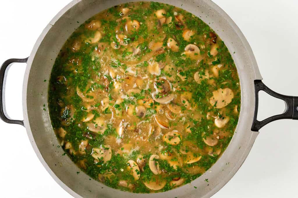 A pot of mushroom stew with sliced mushrooms, herbs, and a light broth. The dish resembles smothered pork chops with its rich flavors and is garnished with finely chopped parsley for a fresh, green appearance.