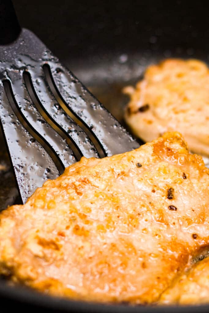 Fried pork chop in oil with herbs and garlic in a cut in the frying pan.