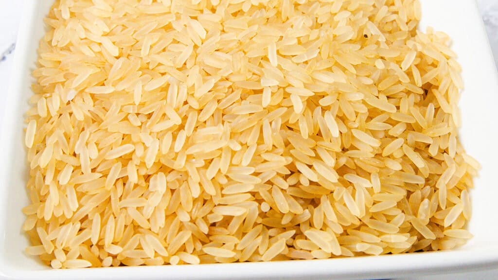 A close-up of uncooked brown rice grains spread evenly on a white rectangular dish, perfect for pairing with savory chicken and yellow rice recipes.