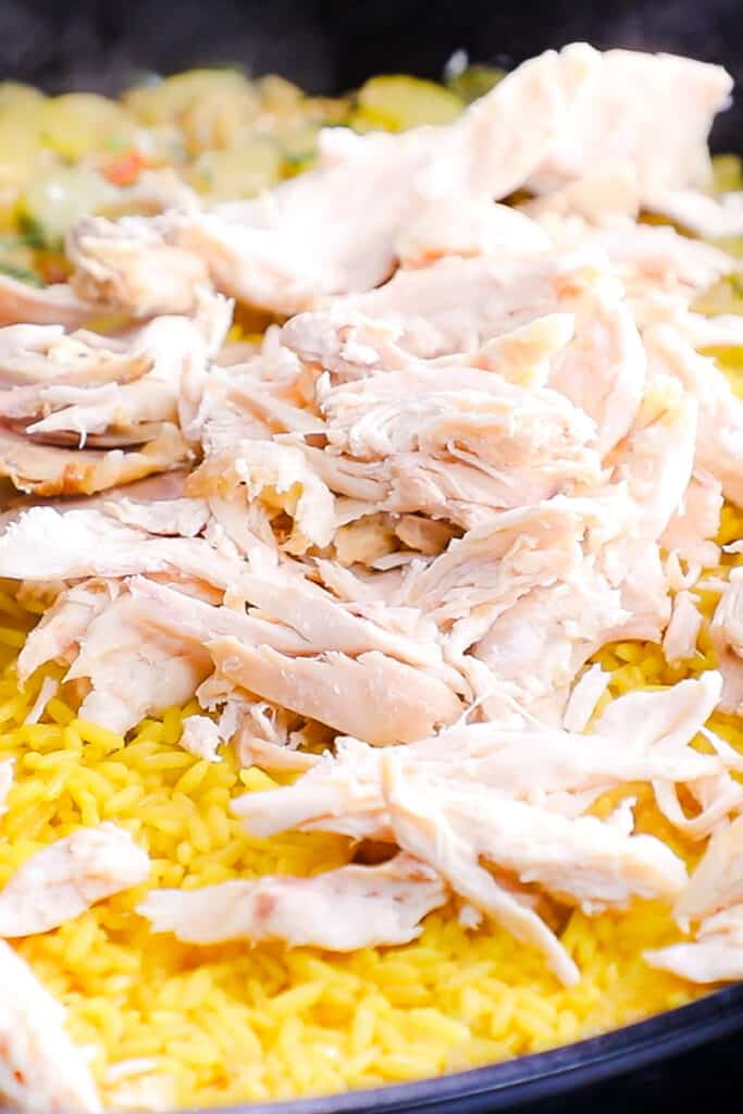 The chicken added to the yellow rice in the pan