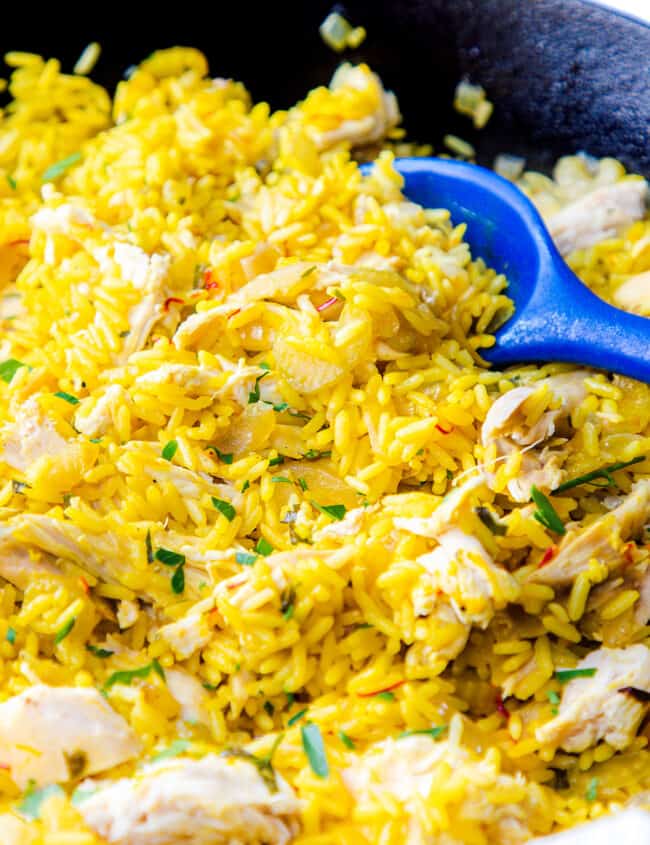 A close up of a pan of chicken and yellow rice with a serving spoon