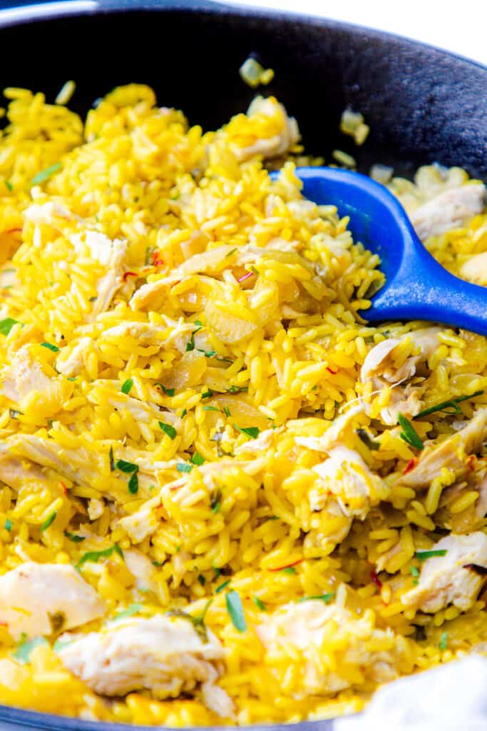 A close up of a pan of chicken and yellow rice with a serving spoon