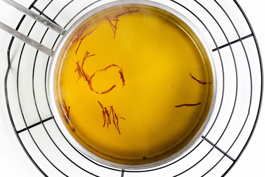 A stainless steel pot with Chicken and Yellow Rice, infused with saffron strands, sits on a round cooling rack, viewed from above against a white background.