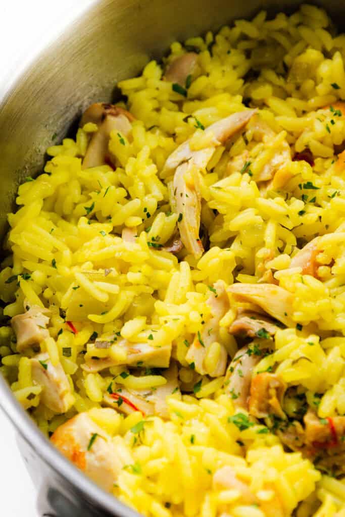 A close-up of a pot filled with flavorful Chicken and Yellow Rice, mixed with tender pieces of chicken and garnished with chopped fresh herbs.