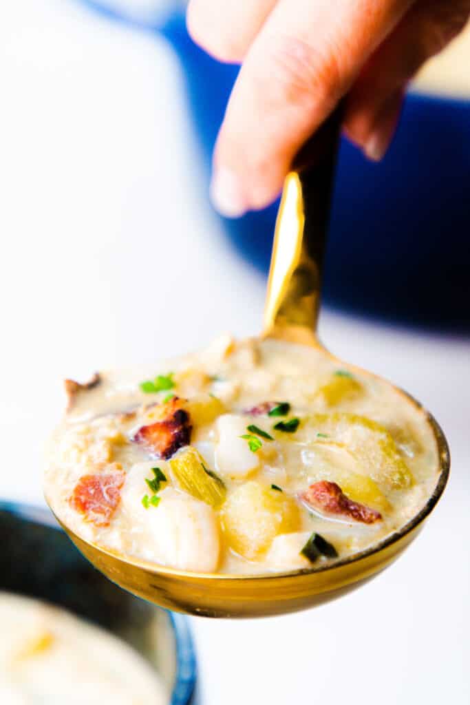 a ladle full of cream of crab soup with potatoes, crab meat, and bacon