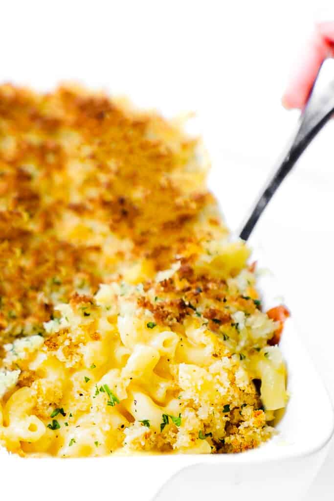 A pan of Creamy Baked Mac & Cheese with a spoon scooping out a portion from the pan