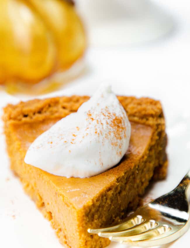 a slice of Pumpkin Pie with Graham Cracker Crust with whipped cream on top and a fork next to it.