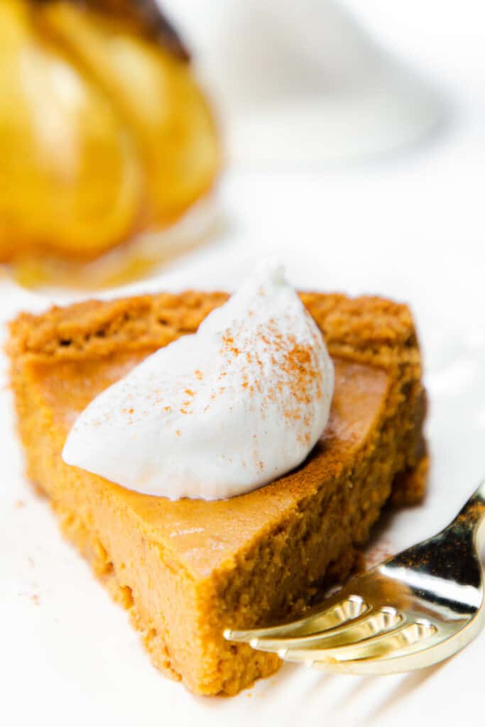 a slice of Pumpkin Pie with Graham Cracker Crust with whipped cream on top and a fork next to it.