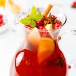 a pitcher of Holiday Sangria with sliced fruit, cranberries, star anise, and a sprig of mint