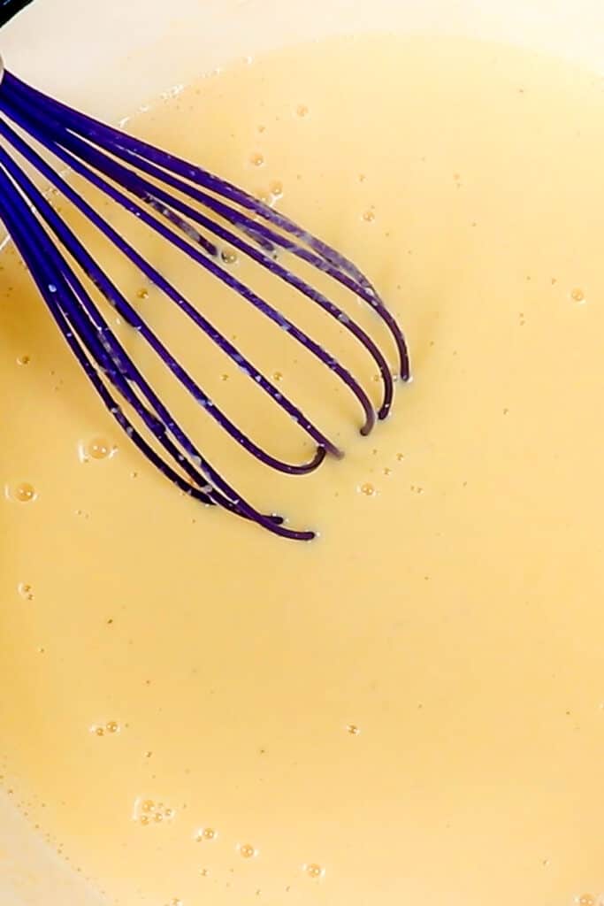 the cheese sauce for Creamy Baked Mac & Cheese in a pot with a whisk