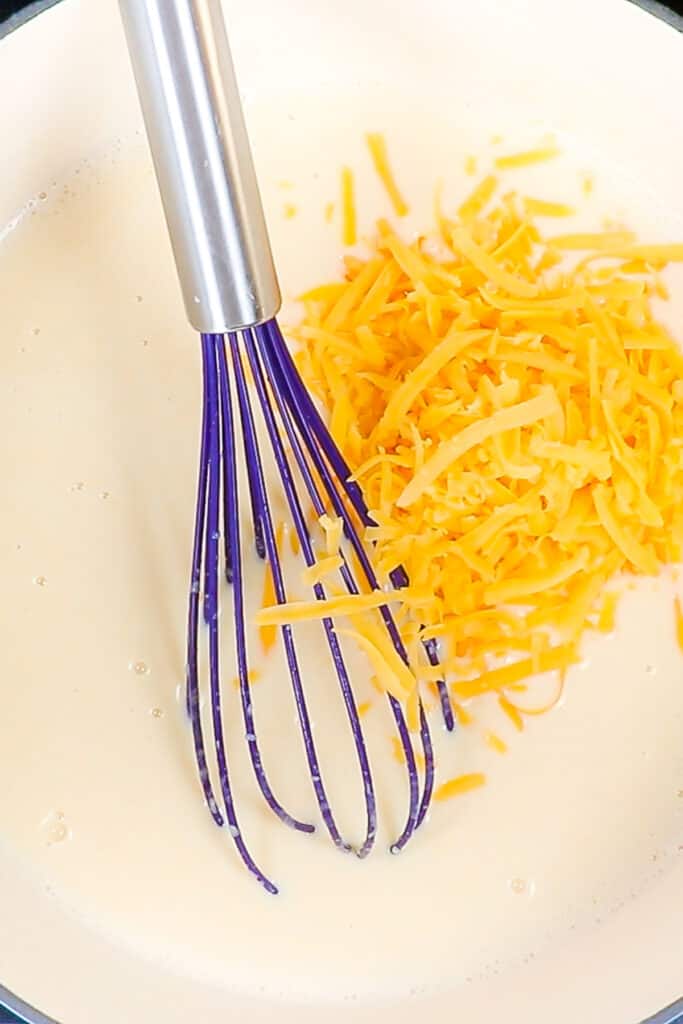 shredded cheddar added to the sauce in a pot with a whisk