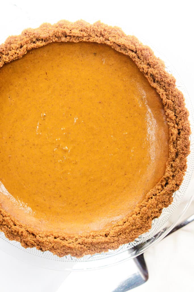 the baked Pumpkin Pie with Graham Cracker Crust on a cake stand with a a pie server next to it